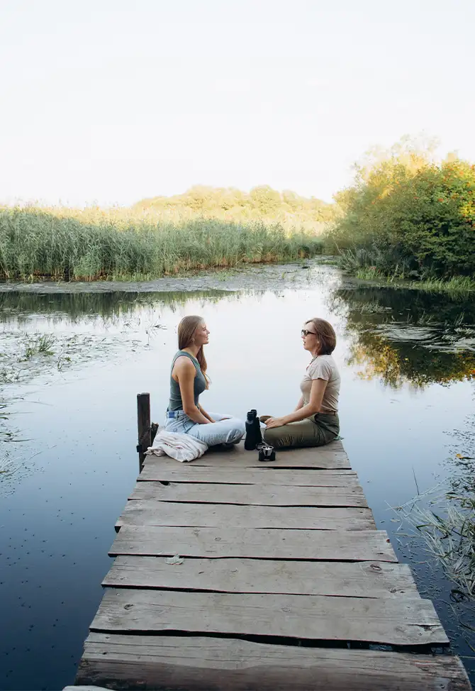 Two women having a calm, thoughtful conversation on a dock by a lake